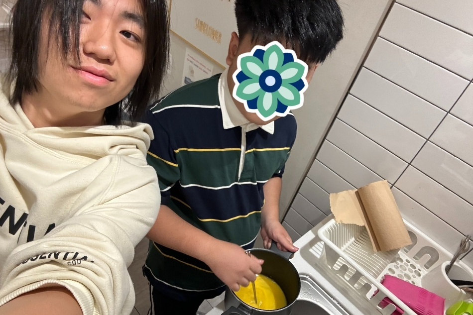 KKOOM volunteer helps a student cook during a hands-on educational activity at camp in Korea. The child’s face is covered with a sticker for privacy.