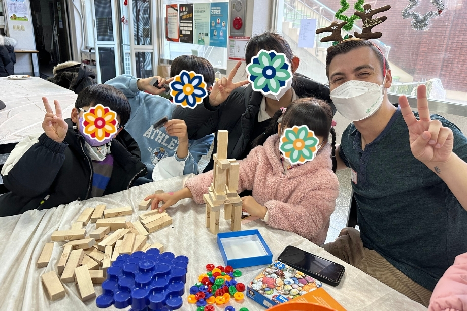 Group of children and volunteer gathered around a table playing with wooden blocks and colorful toys during an indoor activity.